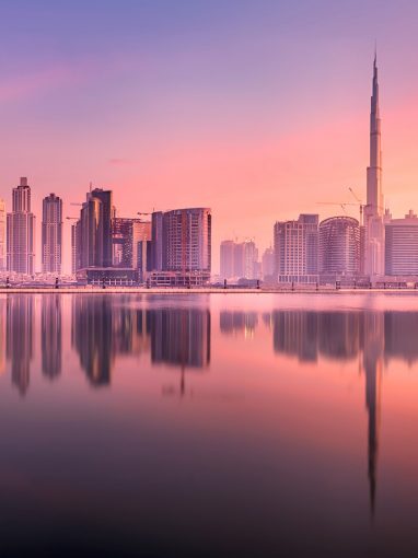 Cityscape of Dubai and panoramic view of Business bay with reflection of skyscrapers on water during purple sunrise, UAE